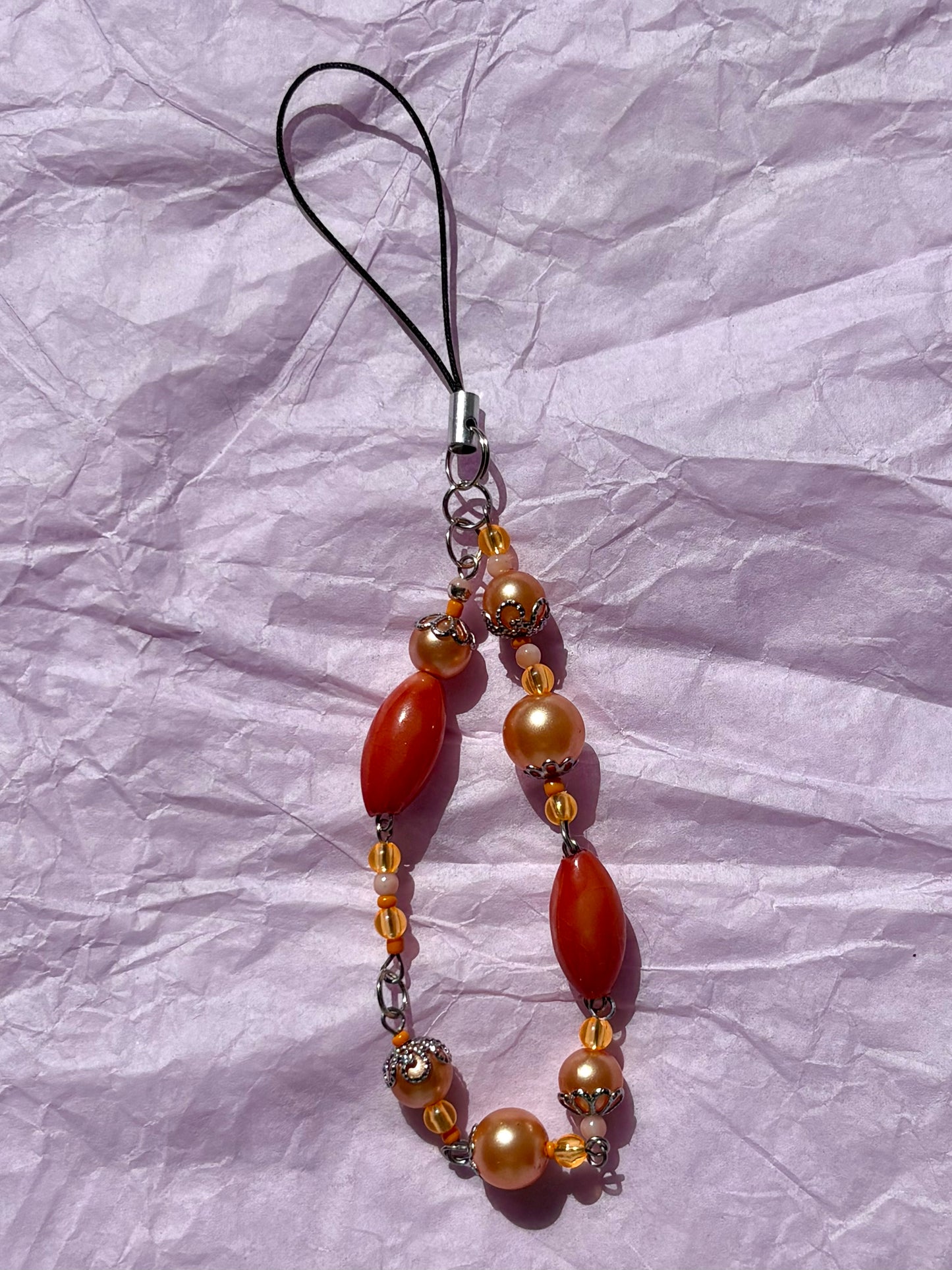 Beaded phone charm with orange and gold beads on a crumpled white background