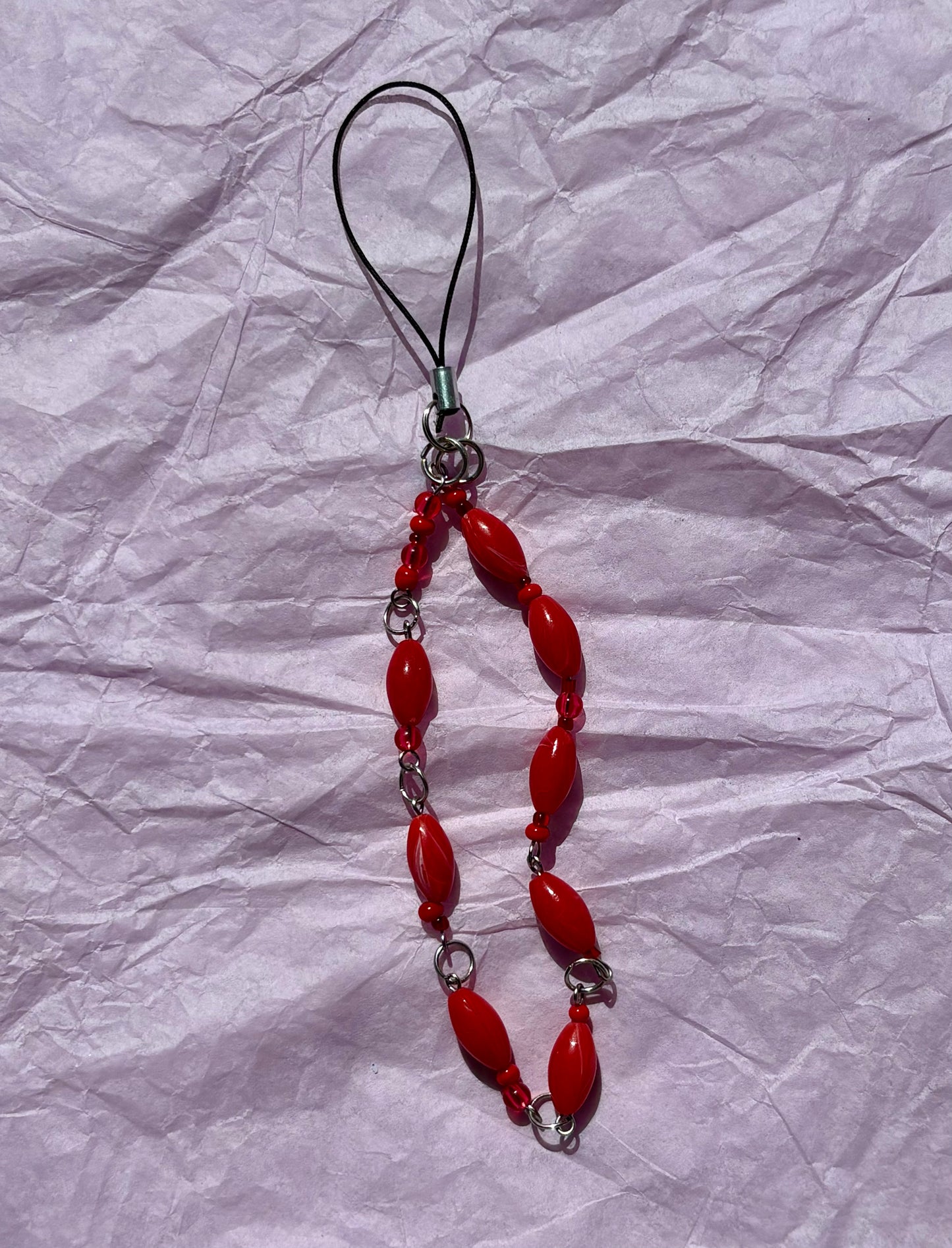 Red beaded phone charm on a crumpled white paper background