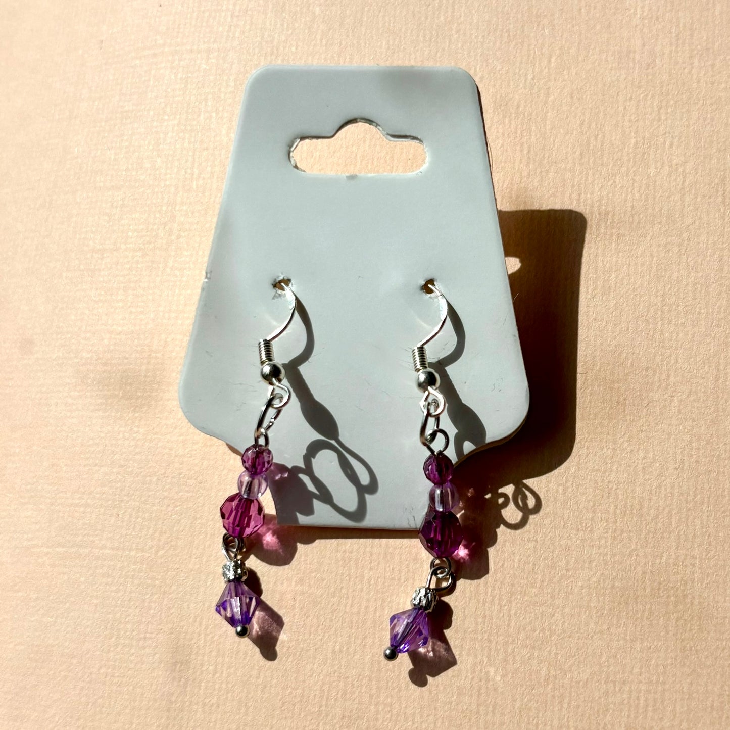 Pair of purple beaded earrings on a gray card against a beige background