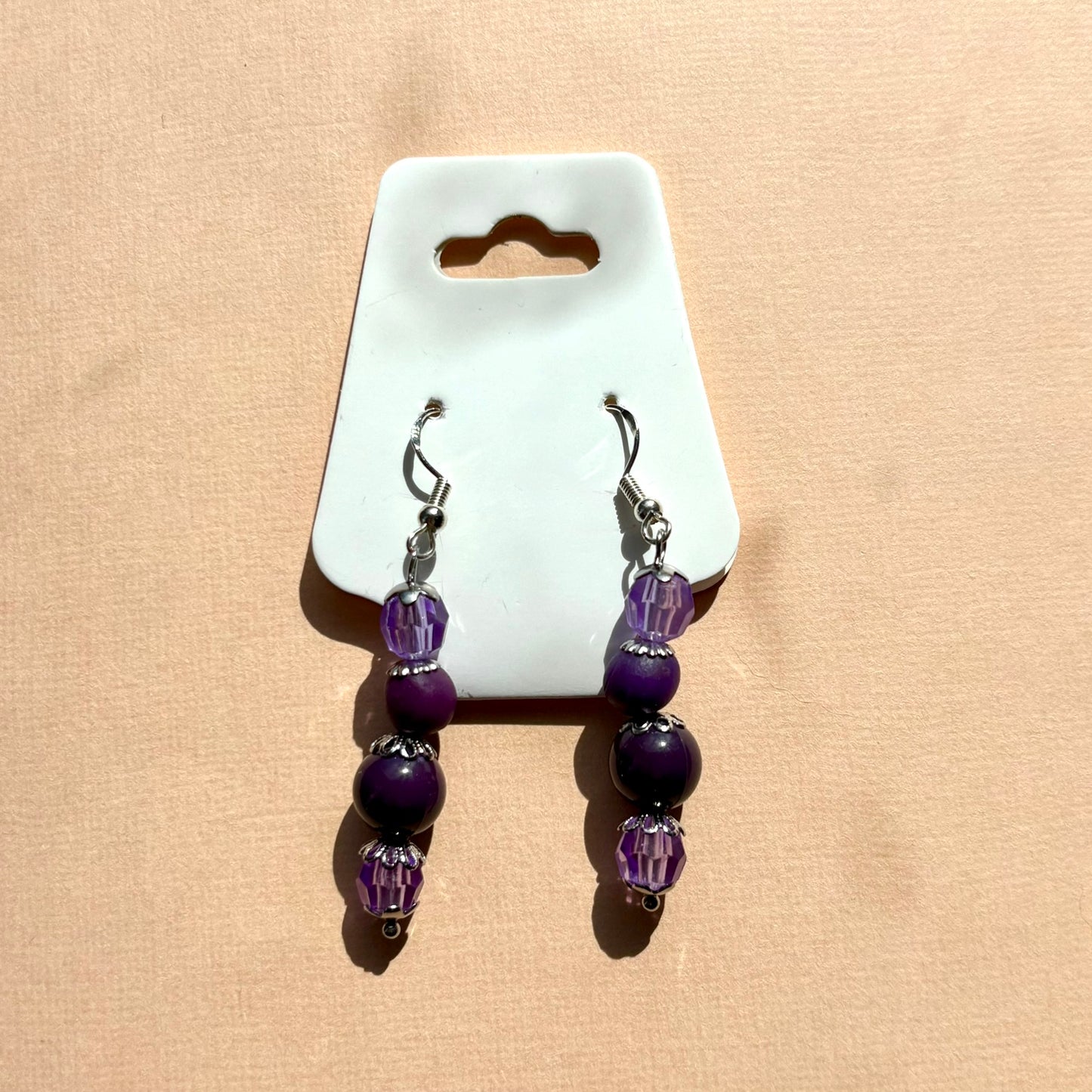 Pair of purple beaded earrings on a white card against a beige background