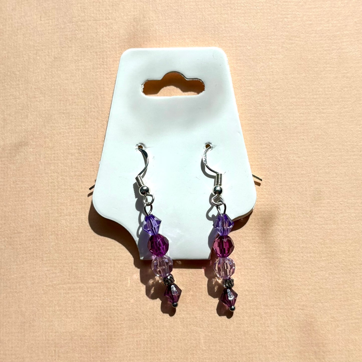 Pair of earrings with purple beads on a white card against a beige background