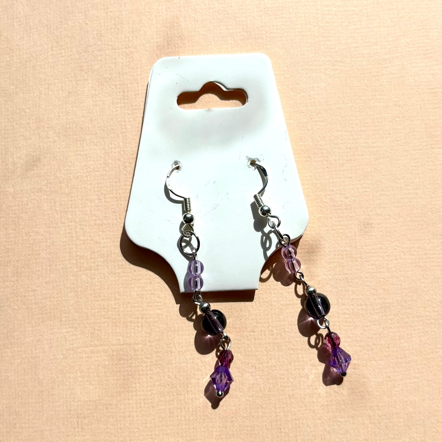 Pair of earrings with purple beads on a white card against a beige background