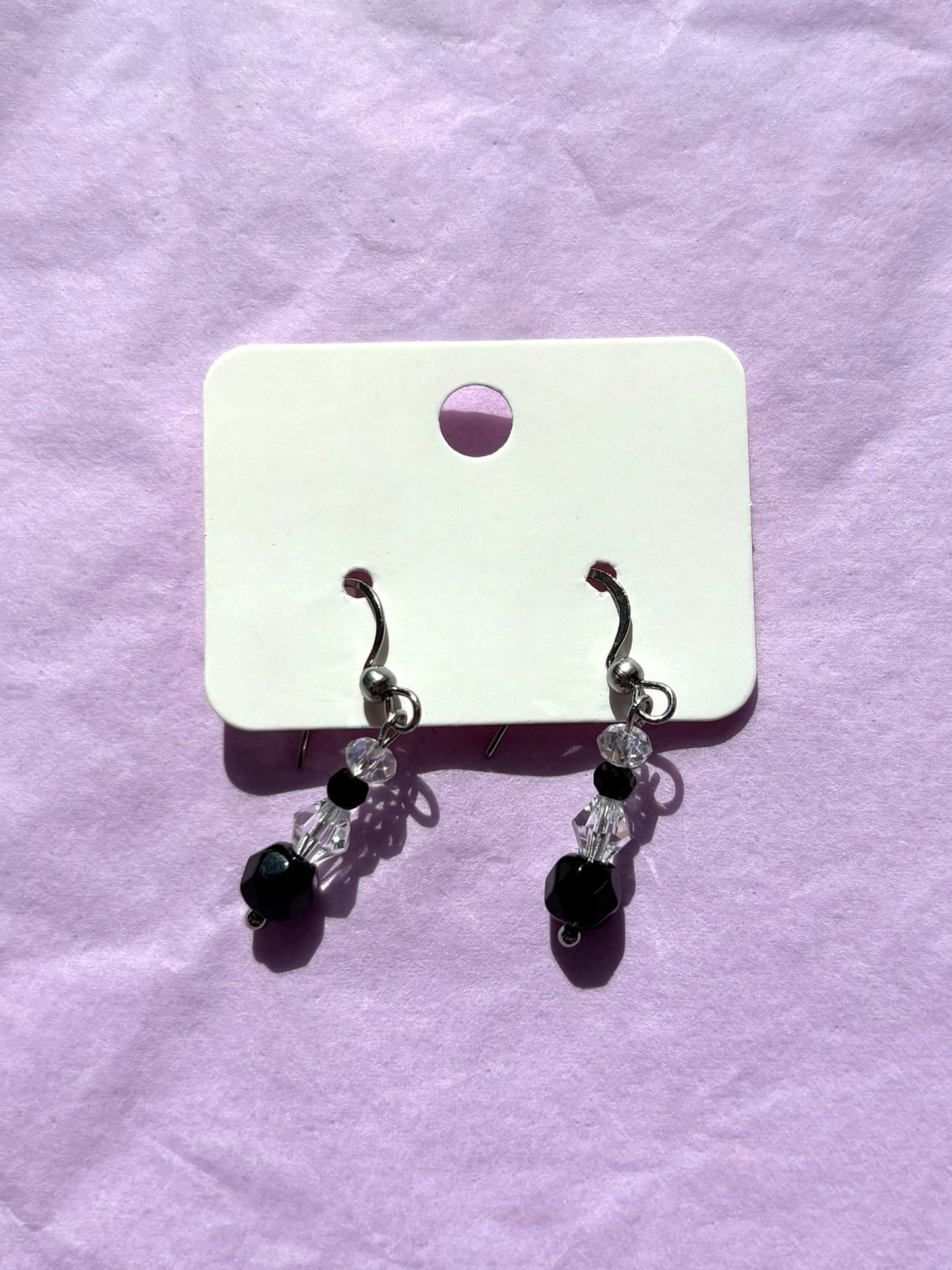 Pair of earrings with black and clear beads on a white card against a purple background