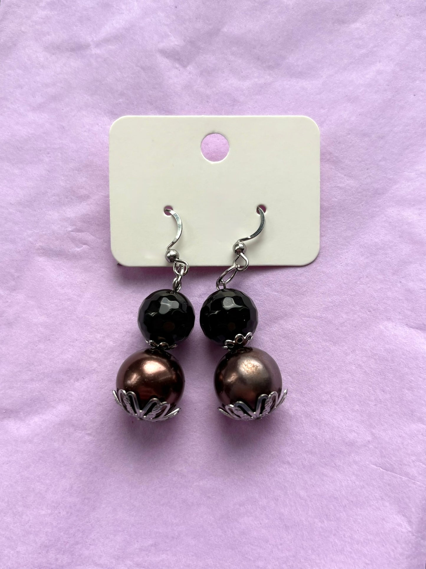 Pair of earrings with black and bronze beads on a purple background