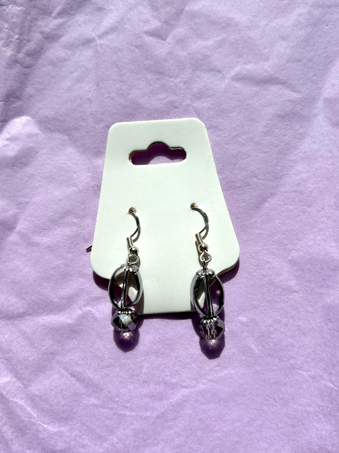 Pair of earrings on a white card with a purple background