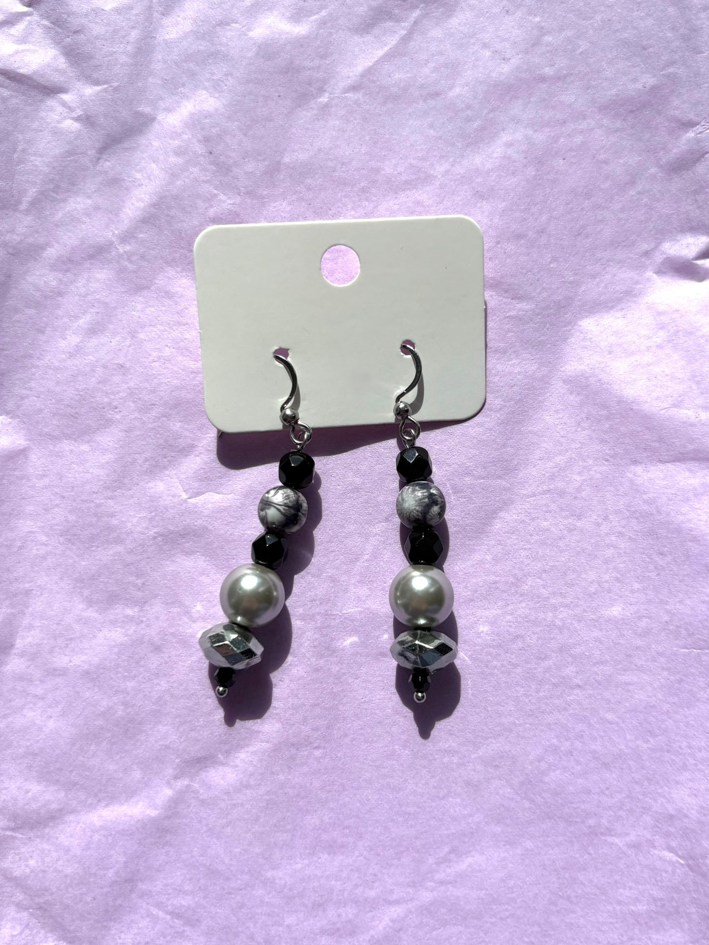 Pair of earrings with pearls and black beads on a white card against a light purple background
