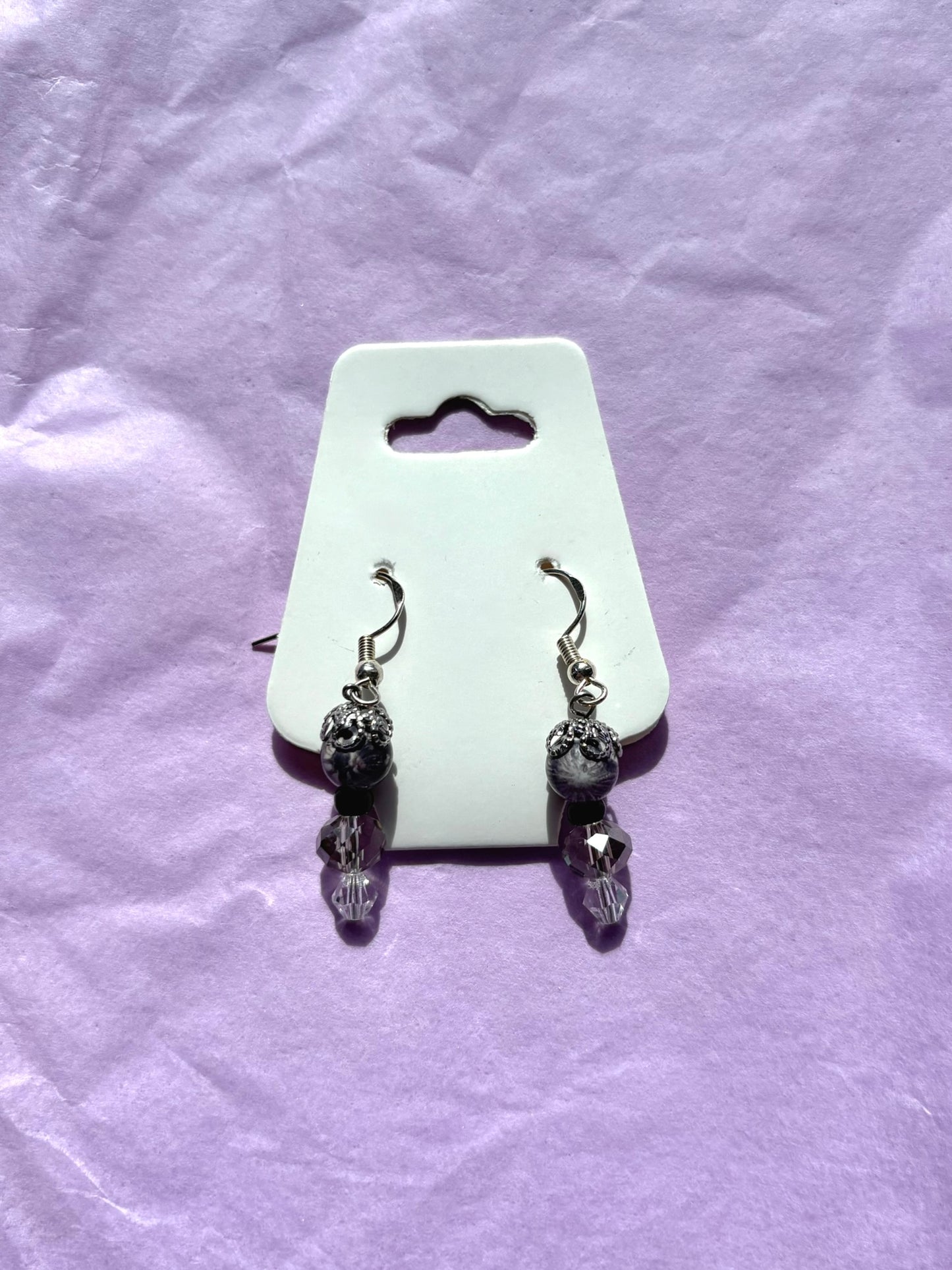 Pair of black beaded earrings on a white card against a purple textured background