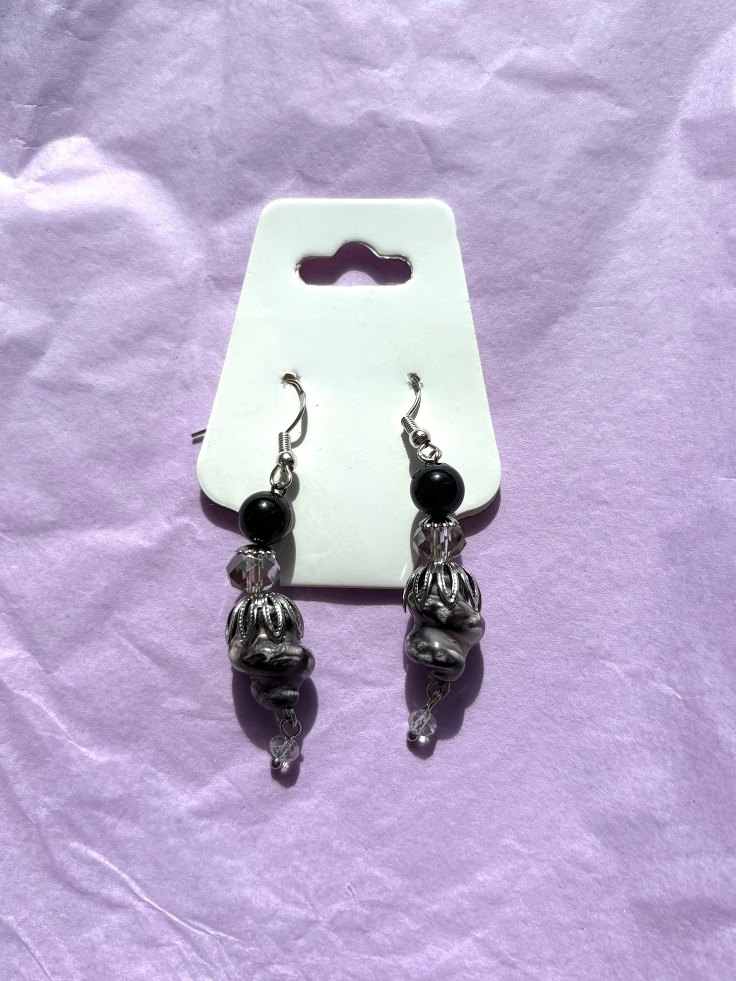 Pair of silver and black beaded earrings on a white card against a purple fabric background