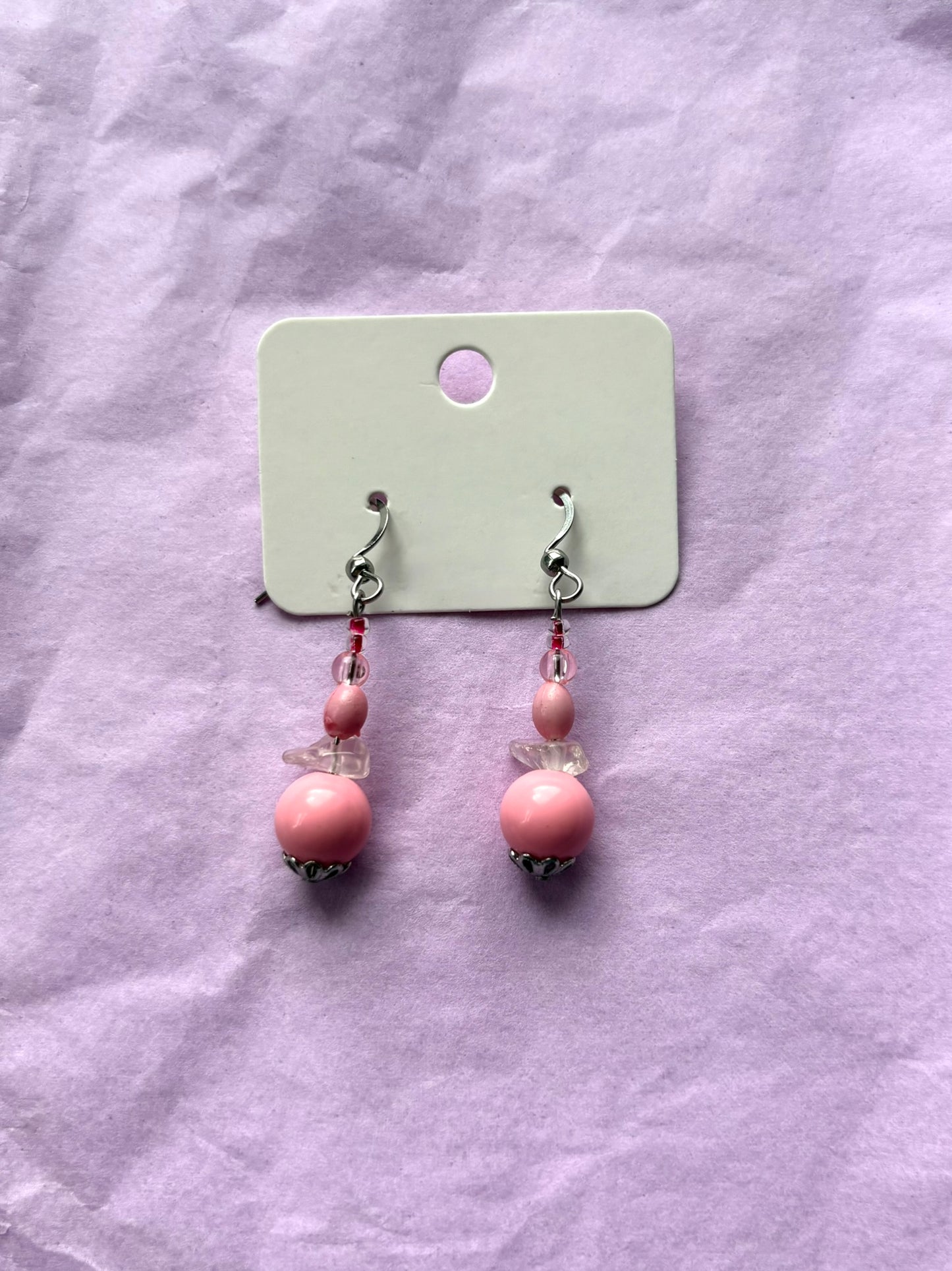 Pair of pink beaded earrings on a light purple fabric background