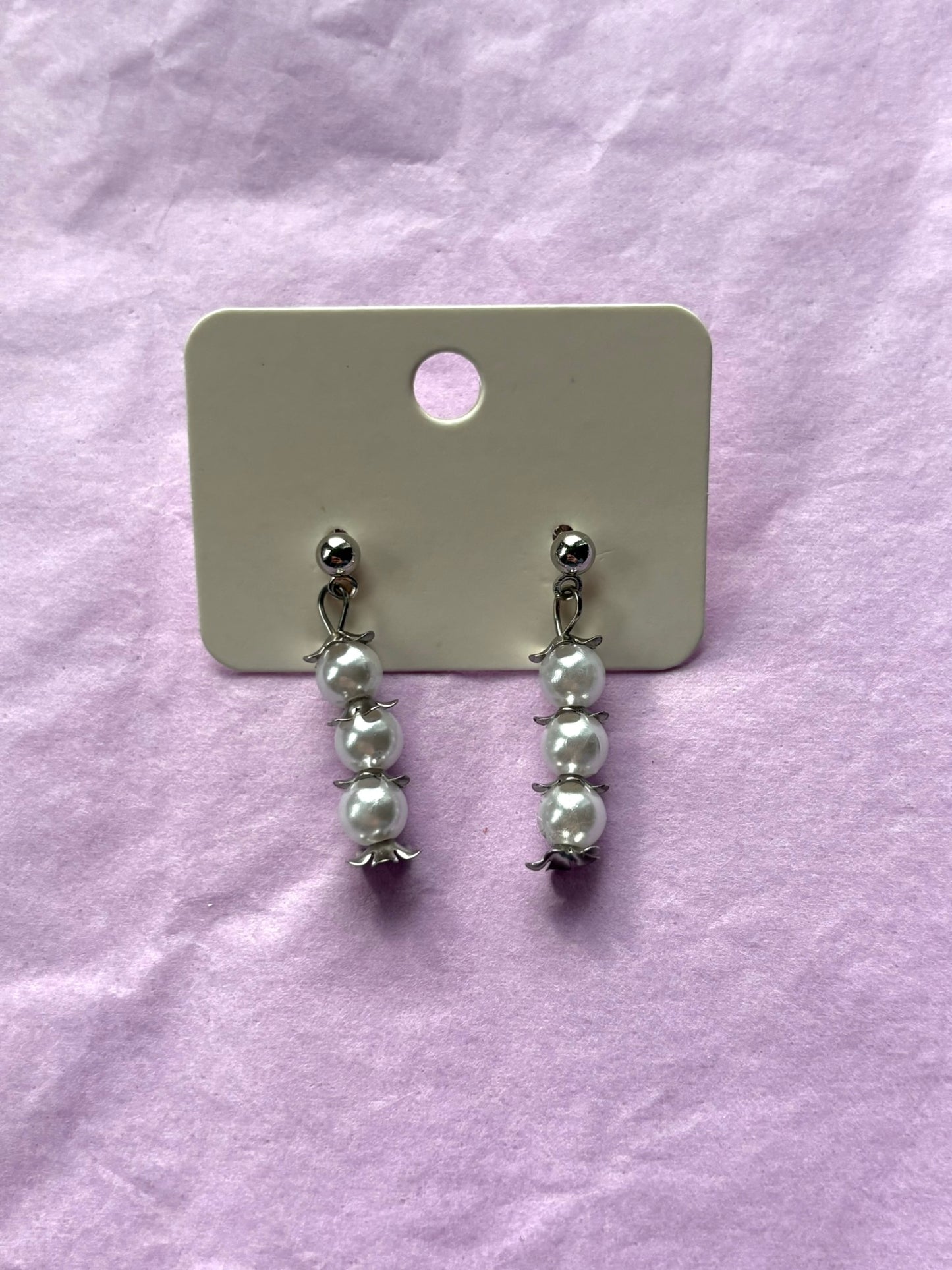 Pair of pearl earrings on a white card against a purple fabric background