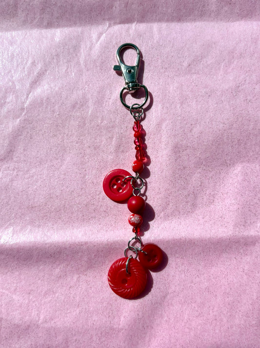 Red button charm keychain on a pink fabric background
