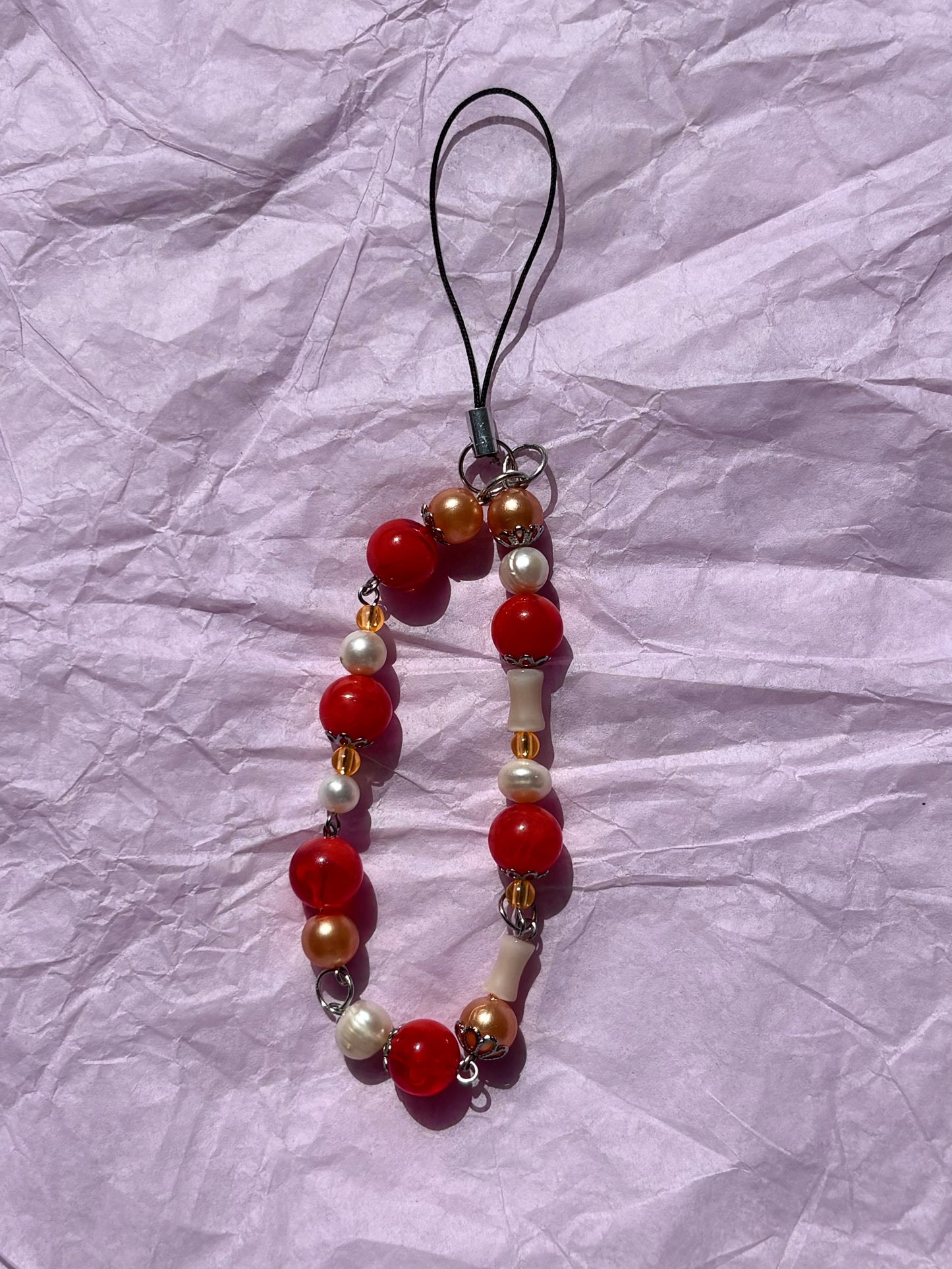 Beaded phone charm with red, gold, and white beads on a crumpled paper background