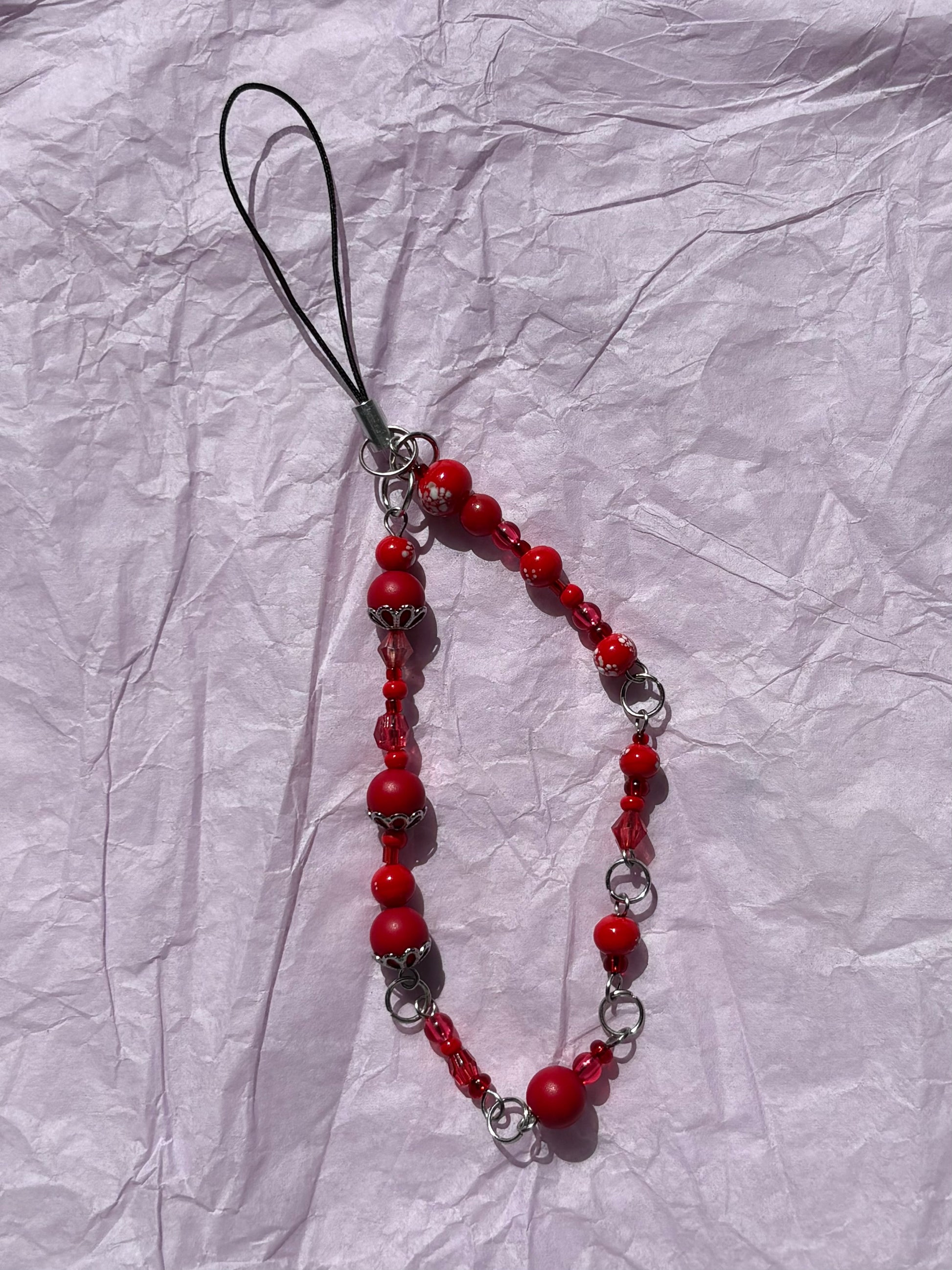 Red beaded phone charm on a crumpled white paper background