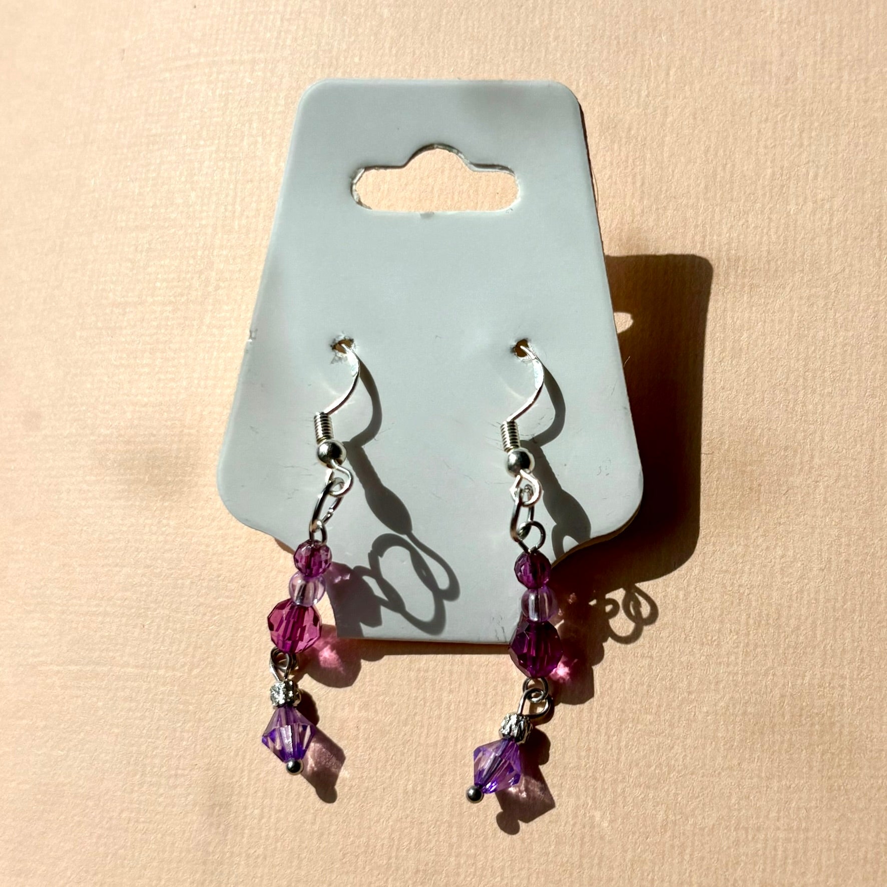 Pair of purple beaded earrings on a gray card against a beige background