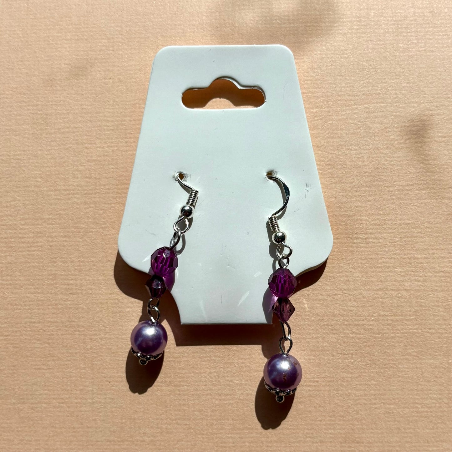 Pair of purple beaded earrings on a white card against a beige background
