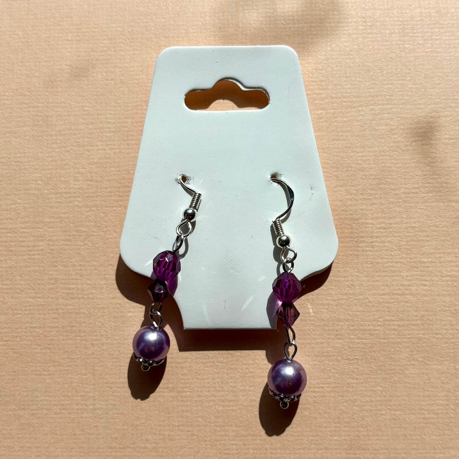 Pair of purple beaded earrings on a white card against a beige background