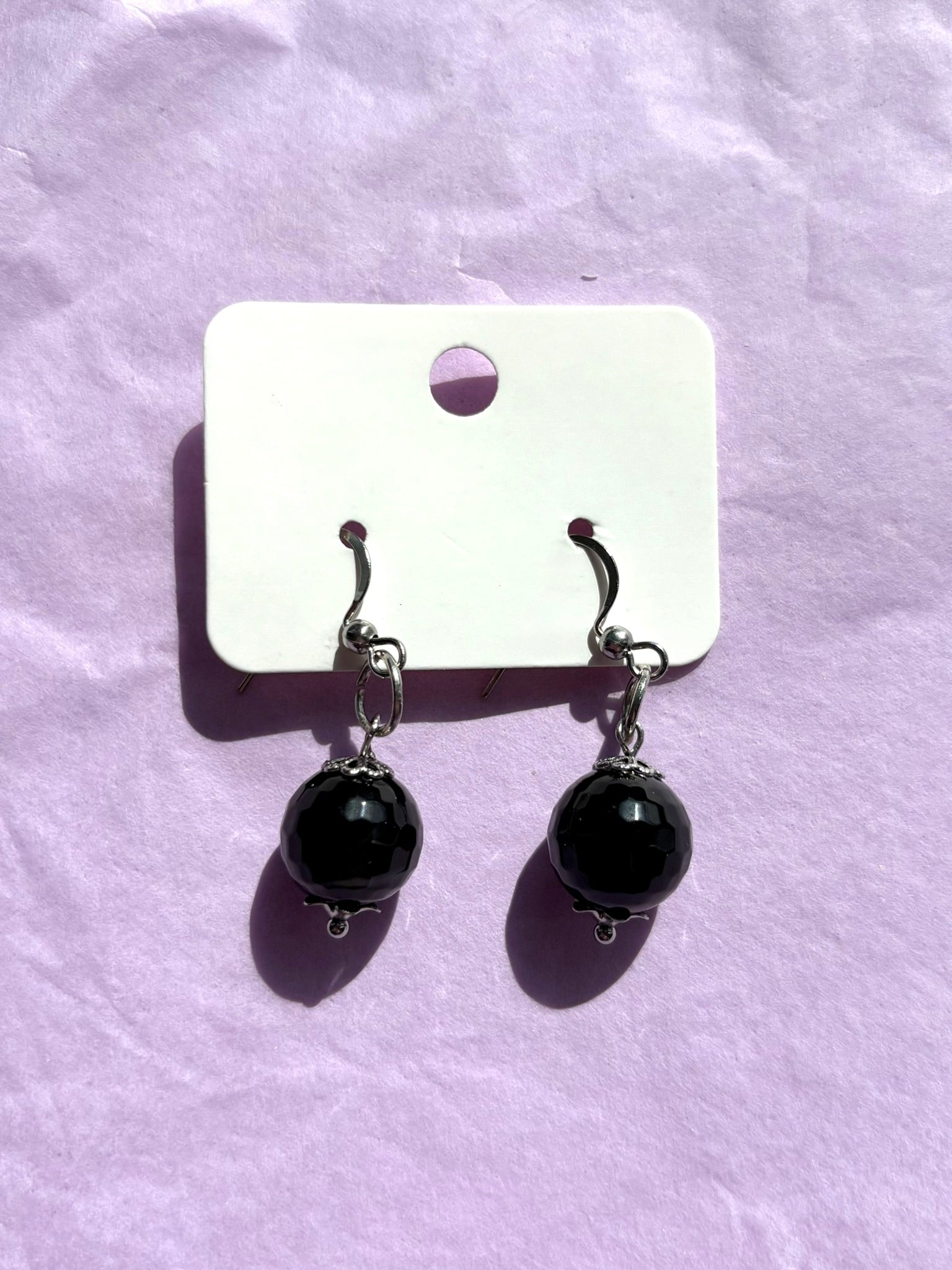 Black beaded earrings on a white card against a purple background