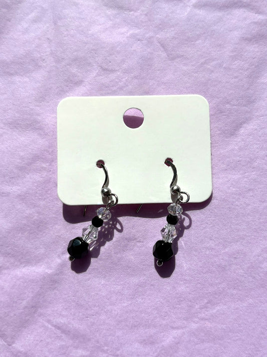 Pair of earrings with black and clear beads on a white card against a purple background