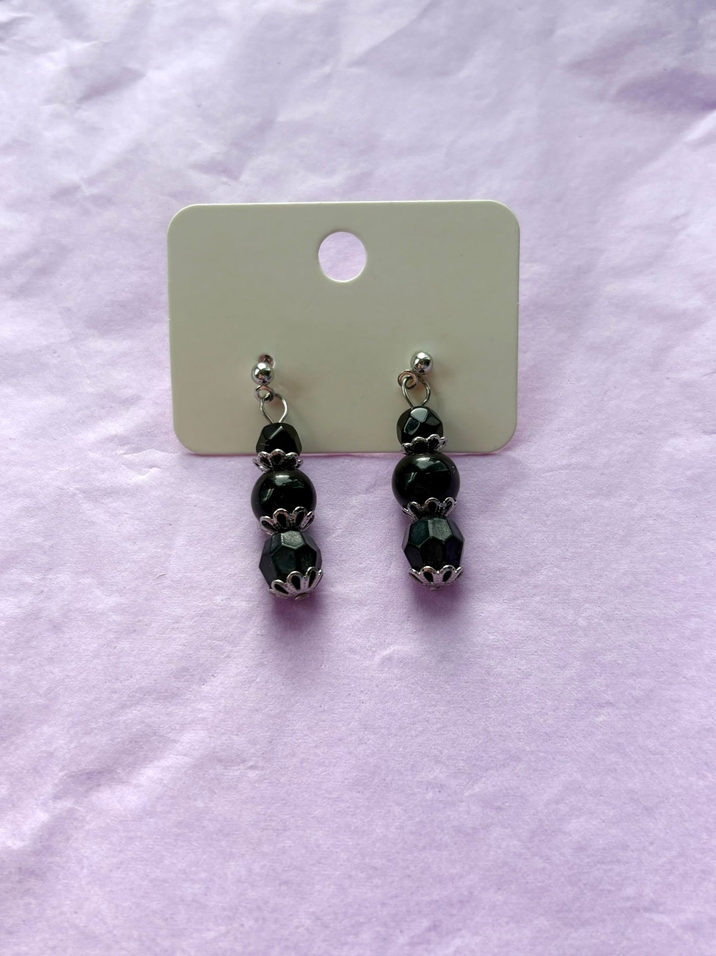 Black beaded earrings on a white card with a white background