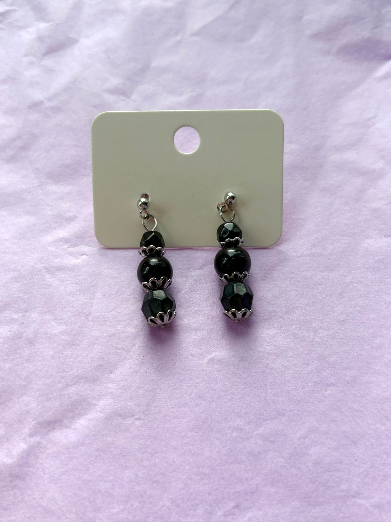 Black beaded earrings on a white card with a white background
