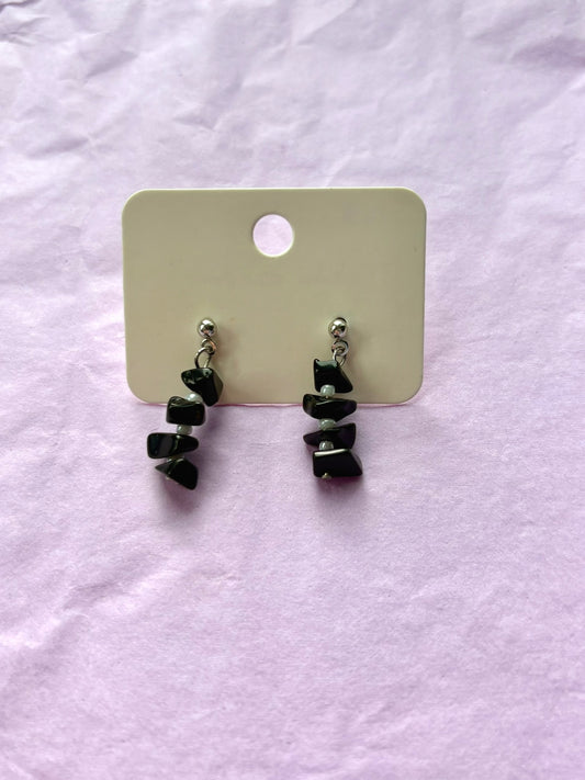 Black beaded earrings on a white card against a light purple background