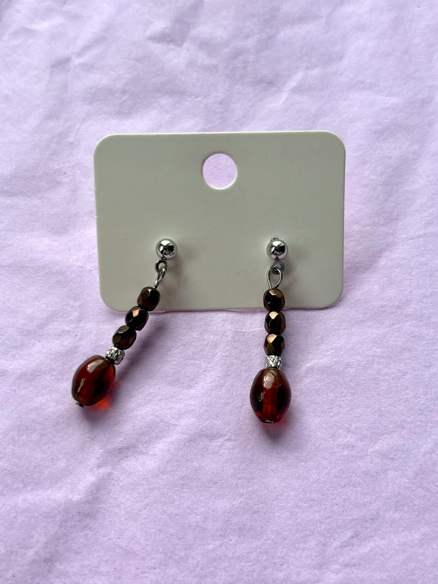Pair of earrings with brown and red beads on a white card against a light purple background