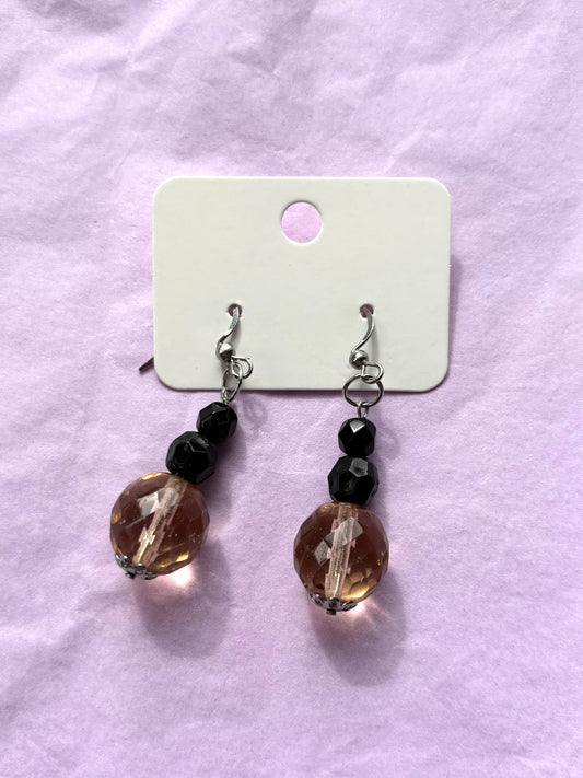 Pair of earrings with brown and black beads on a white card against a pink background