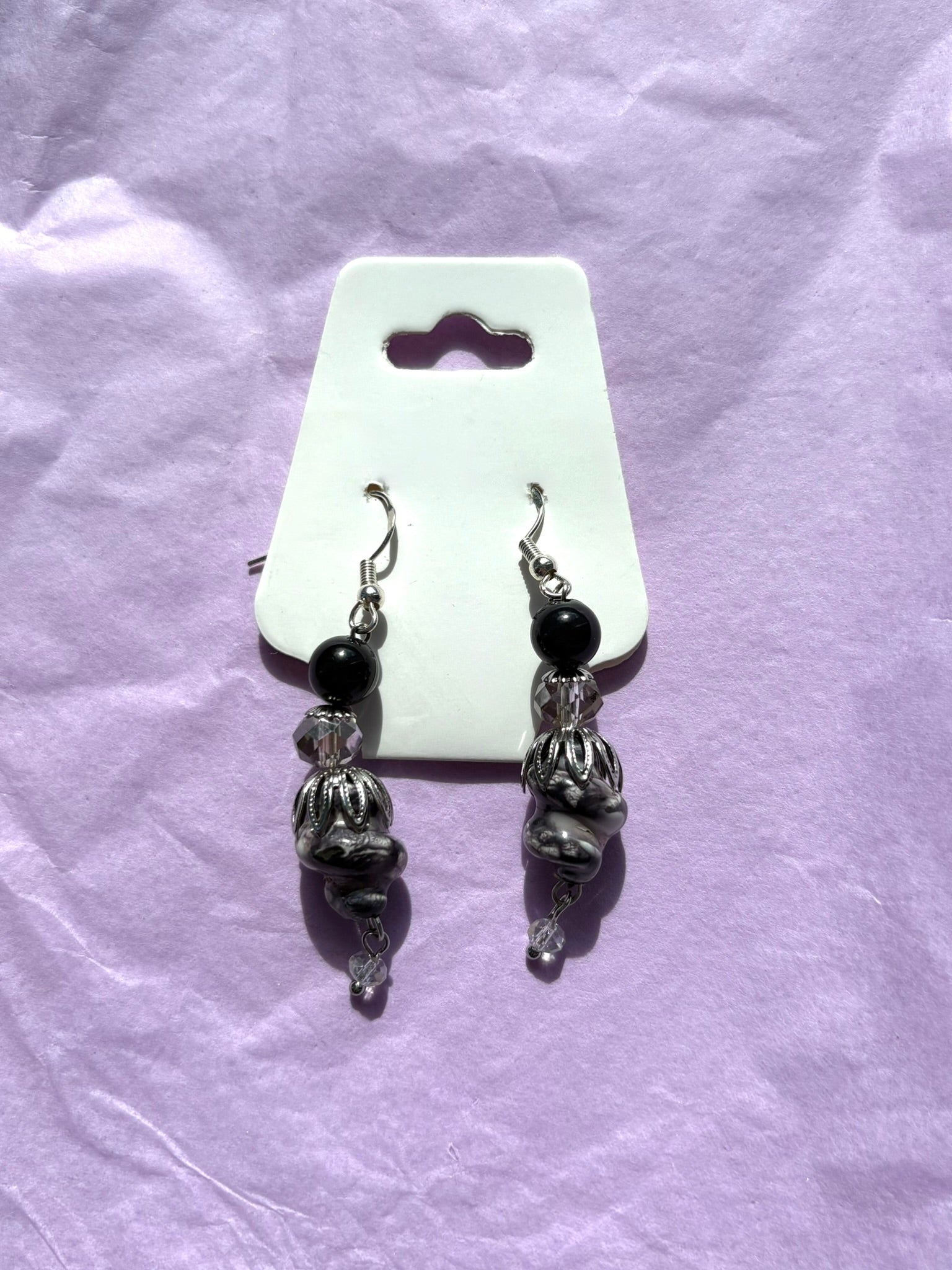 Pair of silver and black beaded earrings on a white card against a purple fabric background