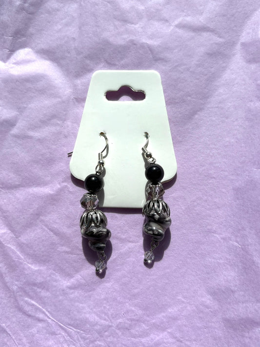 Pair of silver and black beaded earrings on a white card against a purple fabric background