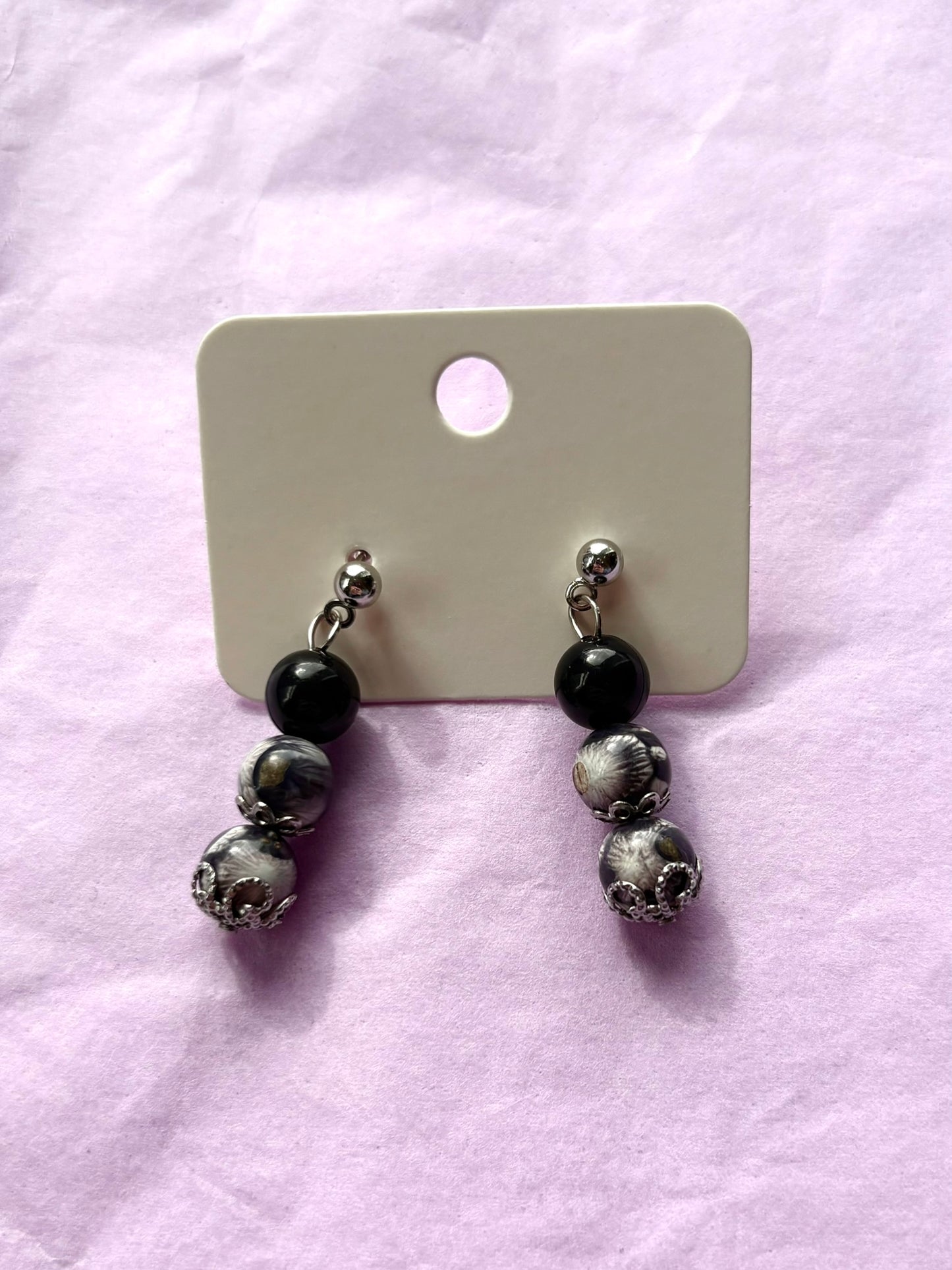 Pair of earrings with black and silver beads on a pink surface