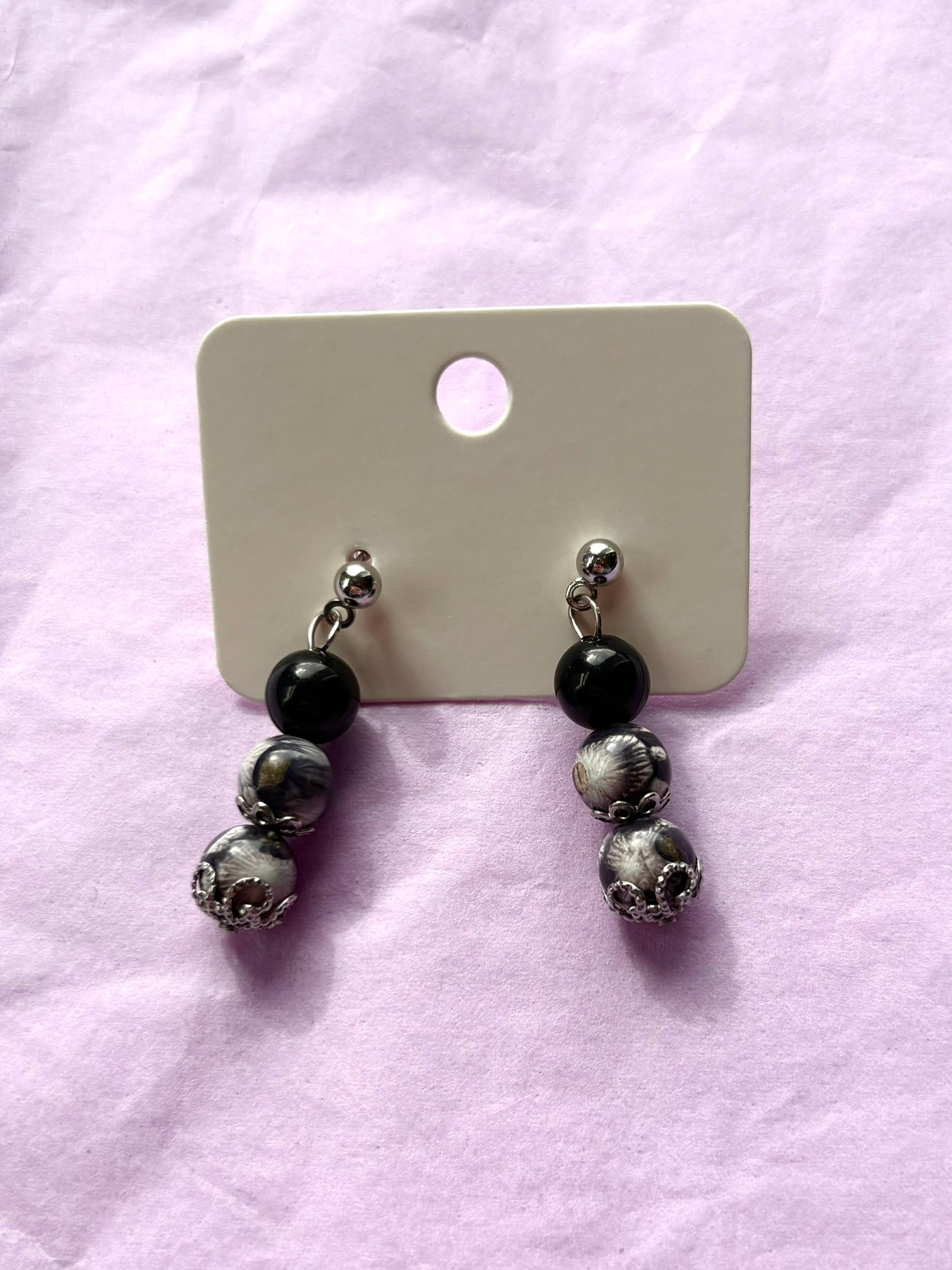 Pair of earrings with black and silver beads on a pink surface
