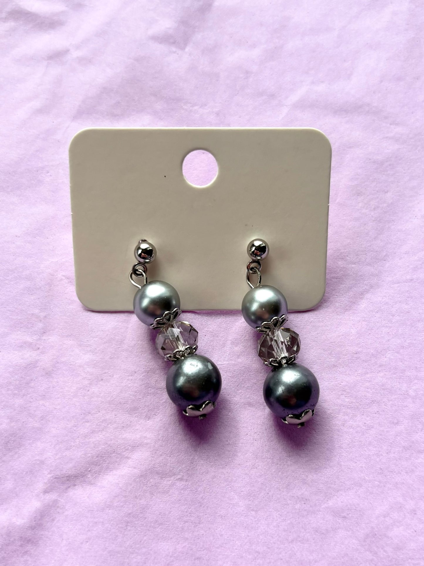 Pair of pearl earrings on a display card against a pink background