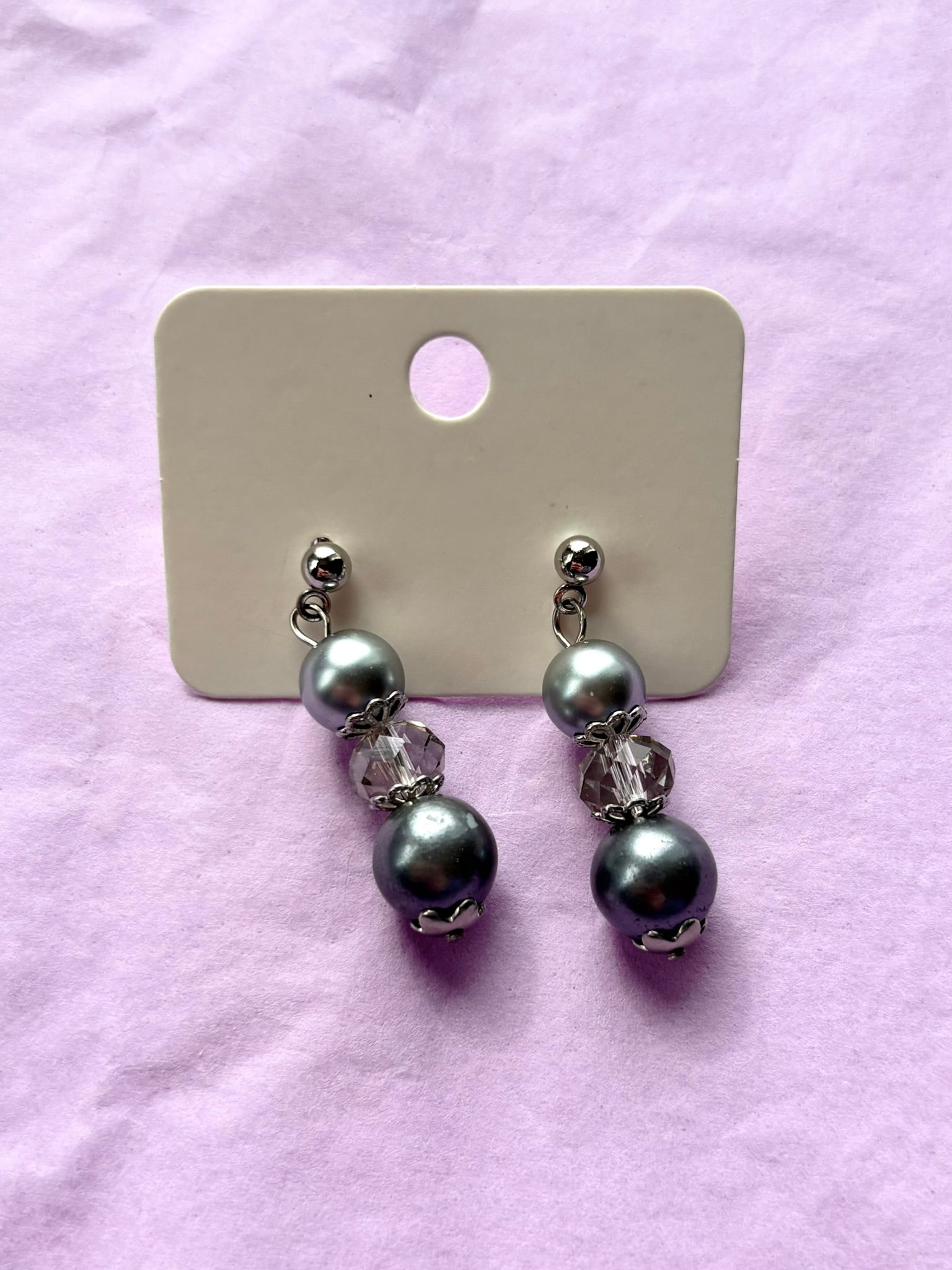 Pair of pearl earrings on a display card against a pink background