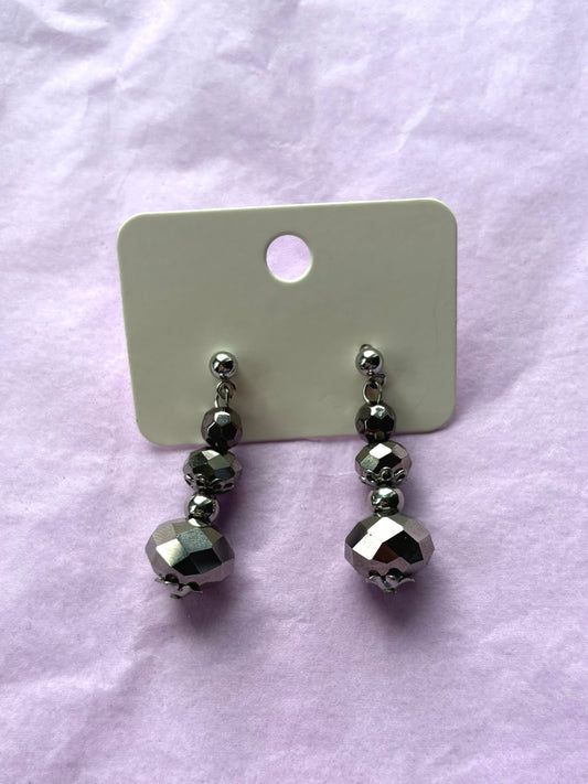 Pair of silver beaded earrings on a white card against a light purple background