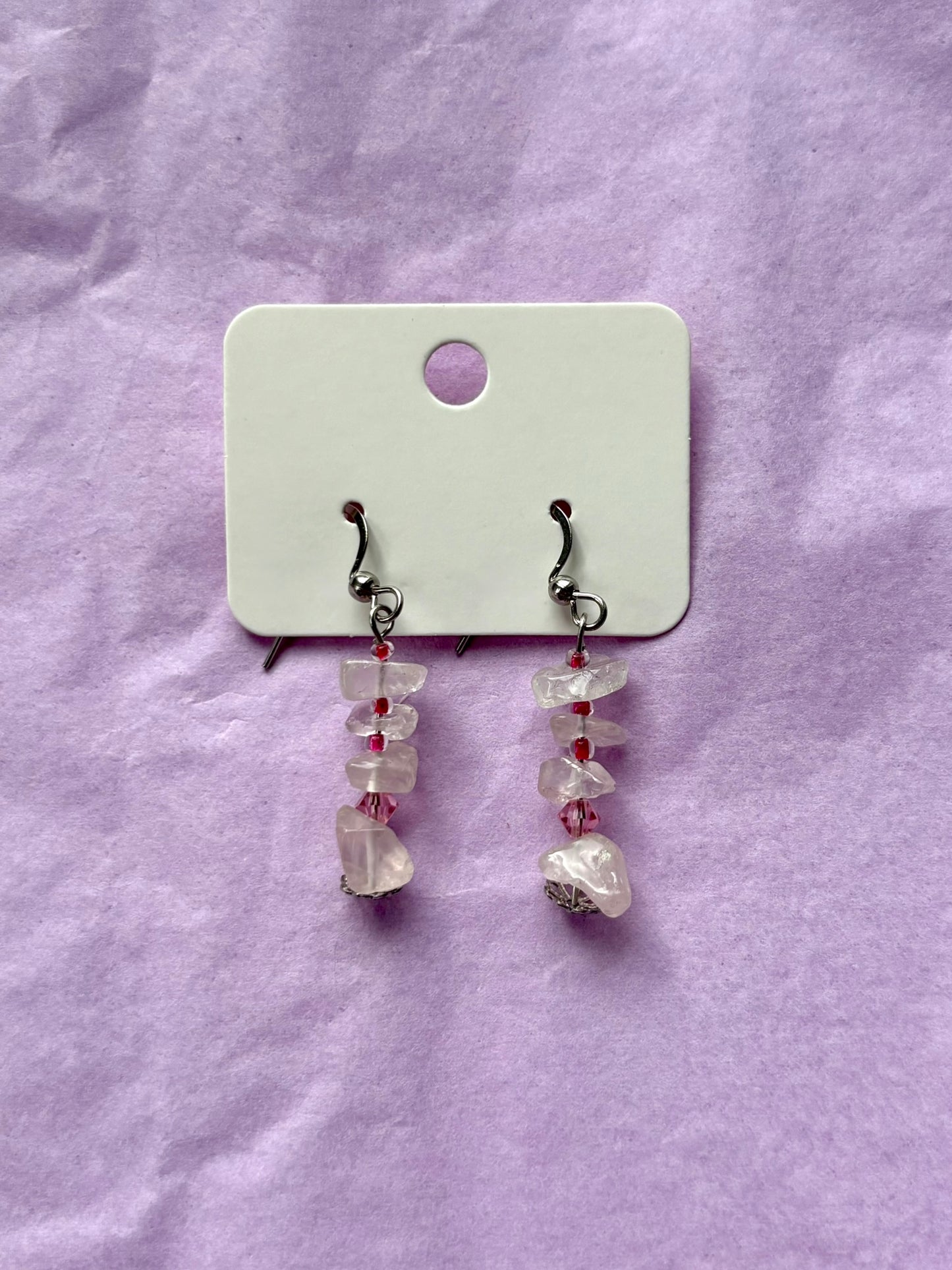 Pair of earrings with clear and red beads on a white card against a purple background
