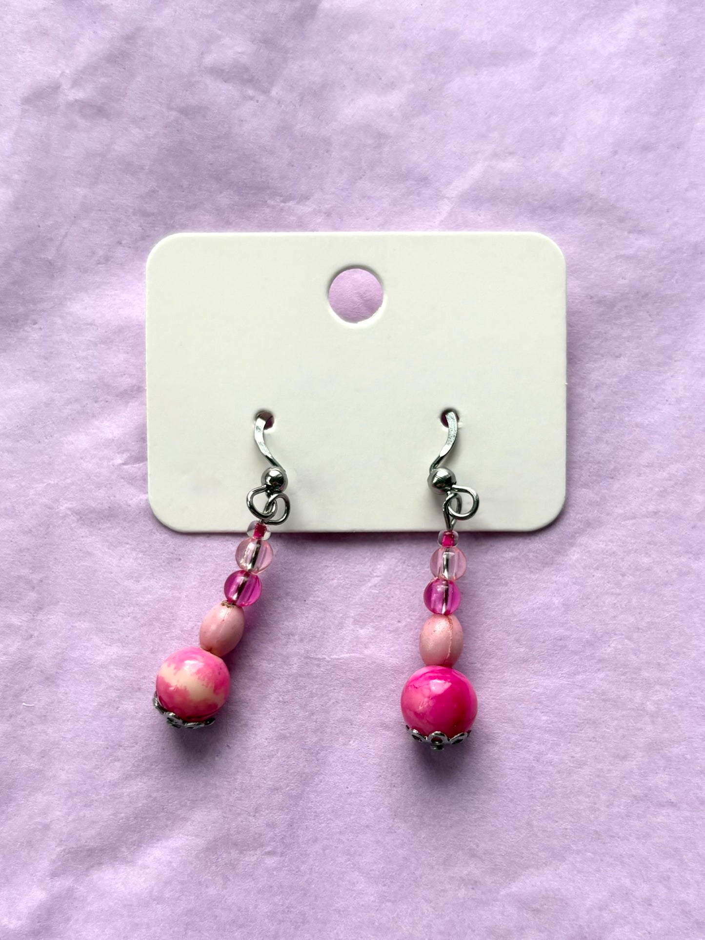 Pink beaded earrings on a white card against a purple background
