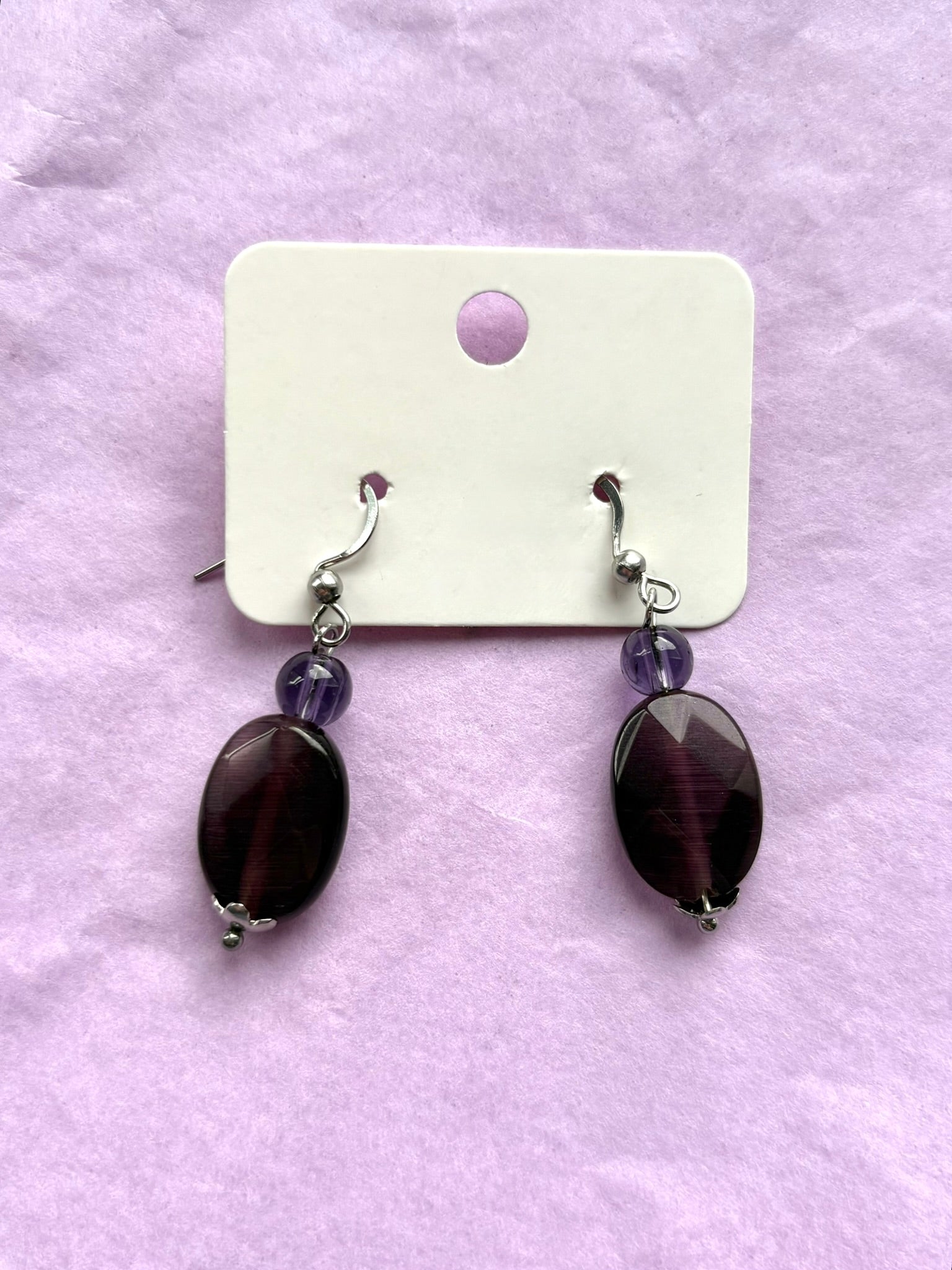 Pair of earrings with purple stones on a white card against a light purple background