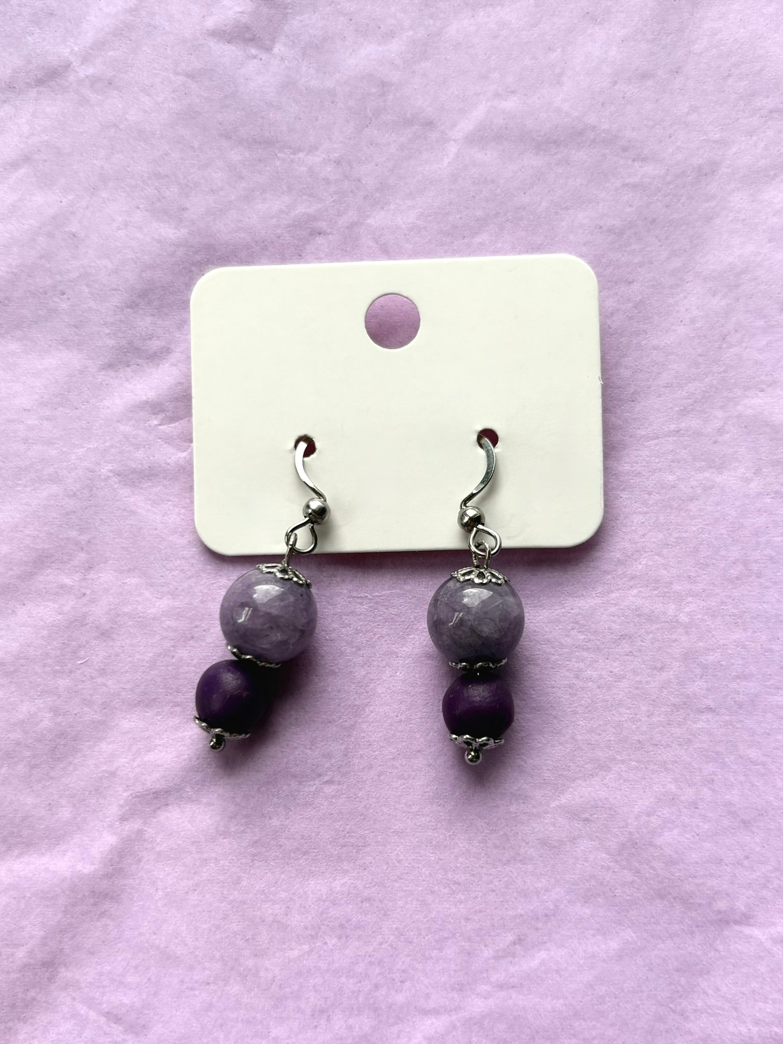 Pair of earrings with purple beads on a white card against a purple background