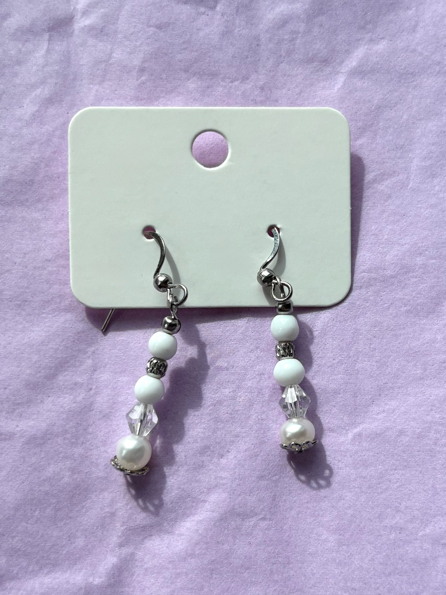 Pair of pearl earrings on a white card against a purple background