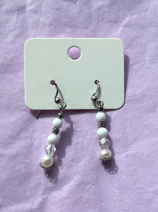 Pair of pearl earrings on a white card against a purple background