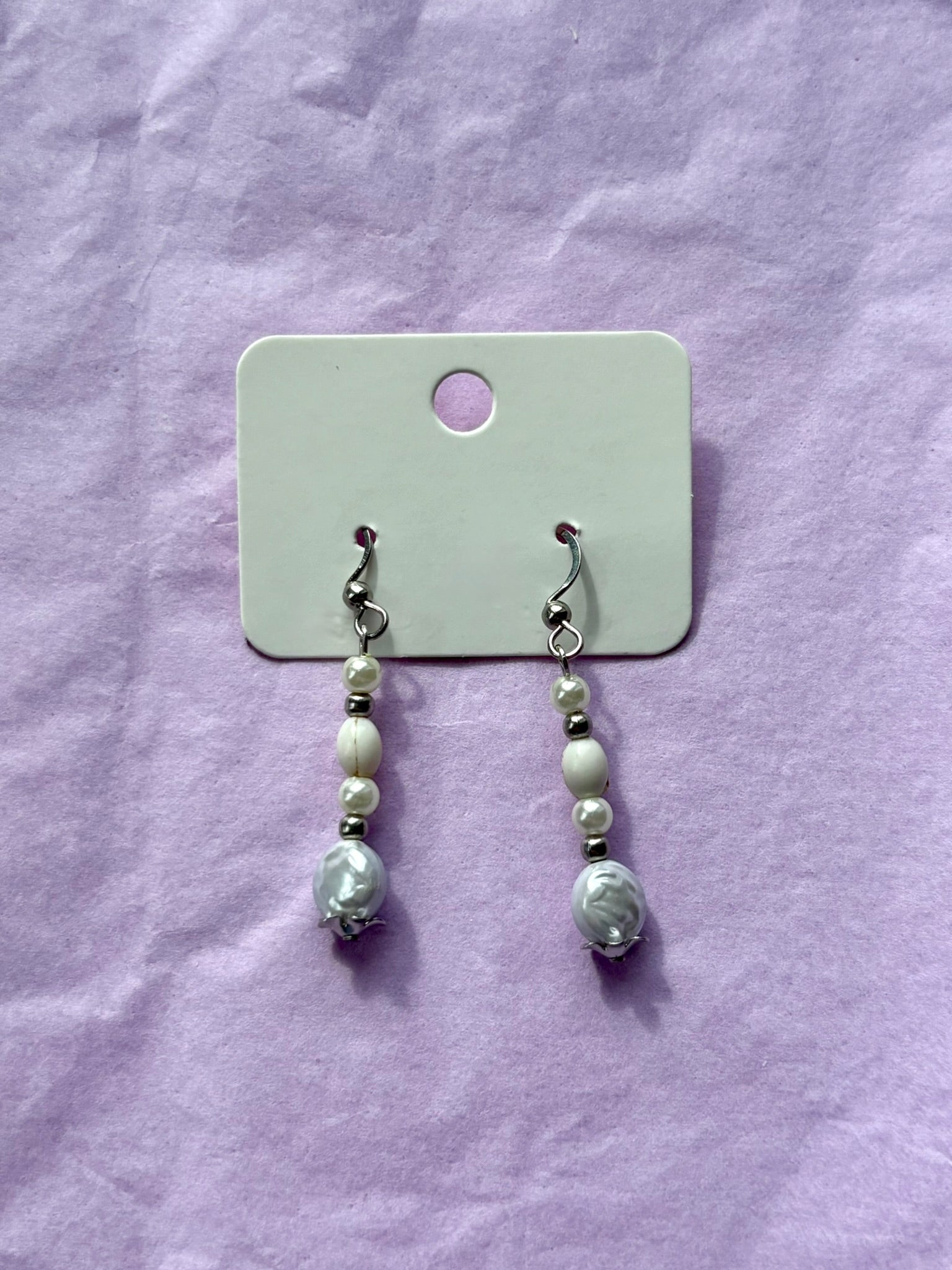 Pair of pearl earrings on a card against a purple fabric background