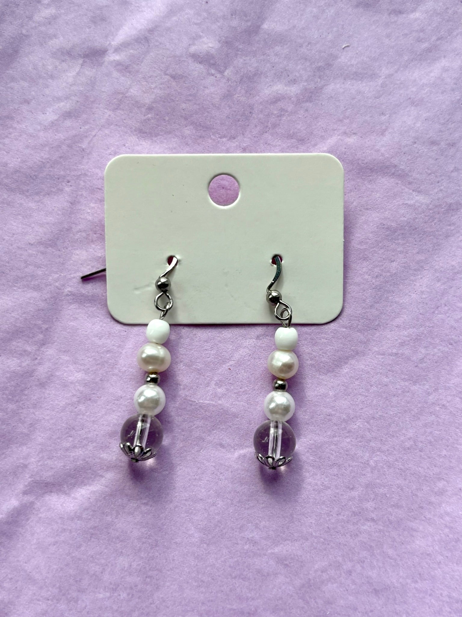 Pair of pearl earrings on a white card against a purple background