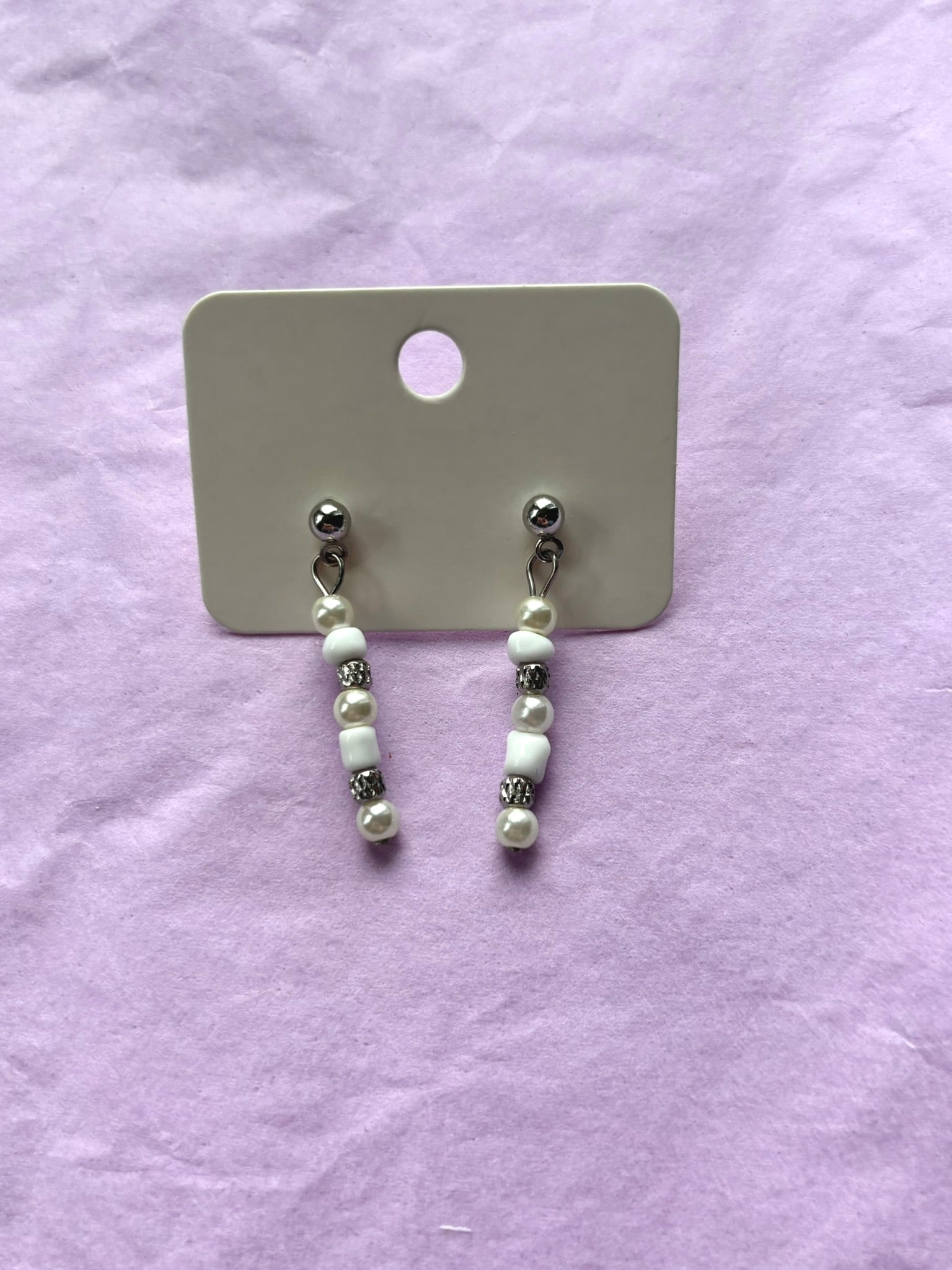 Pair of pearl earrings on a display card against a light purple background