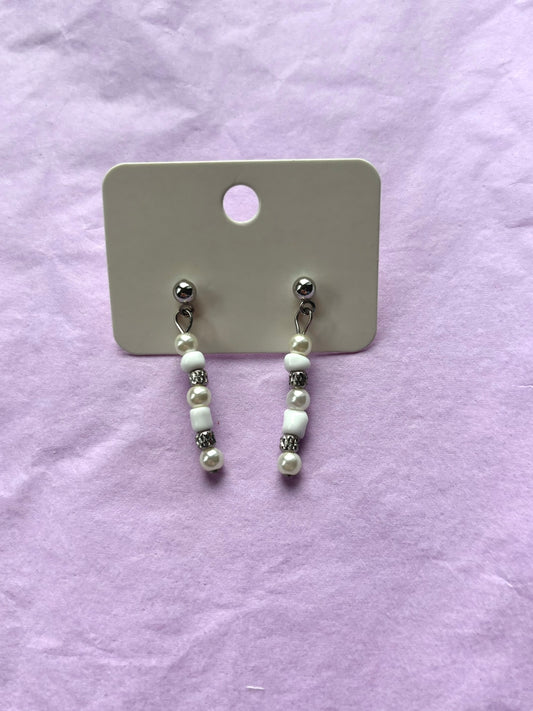 Pair of pearl earrings on a display card against a light purple background
