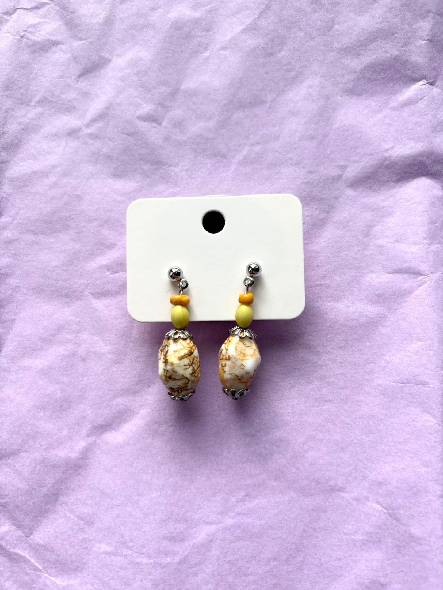 Pair of earrings on a white card against a purple fabric background