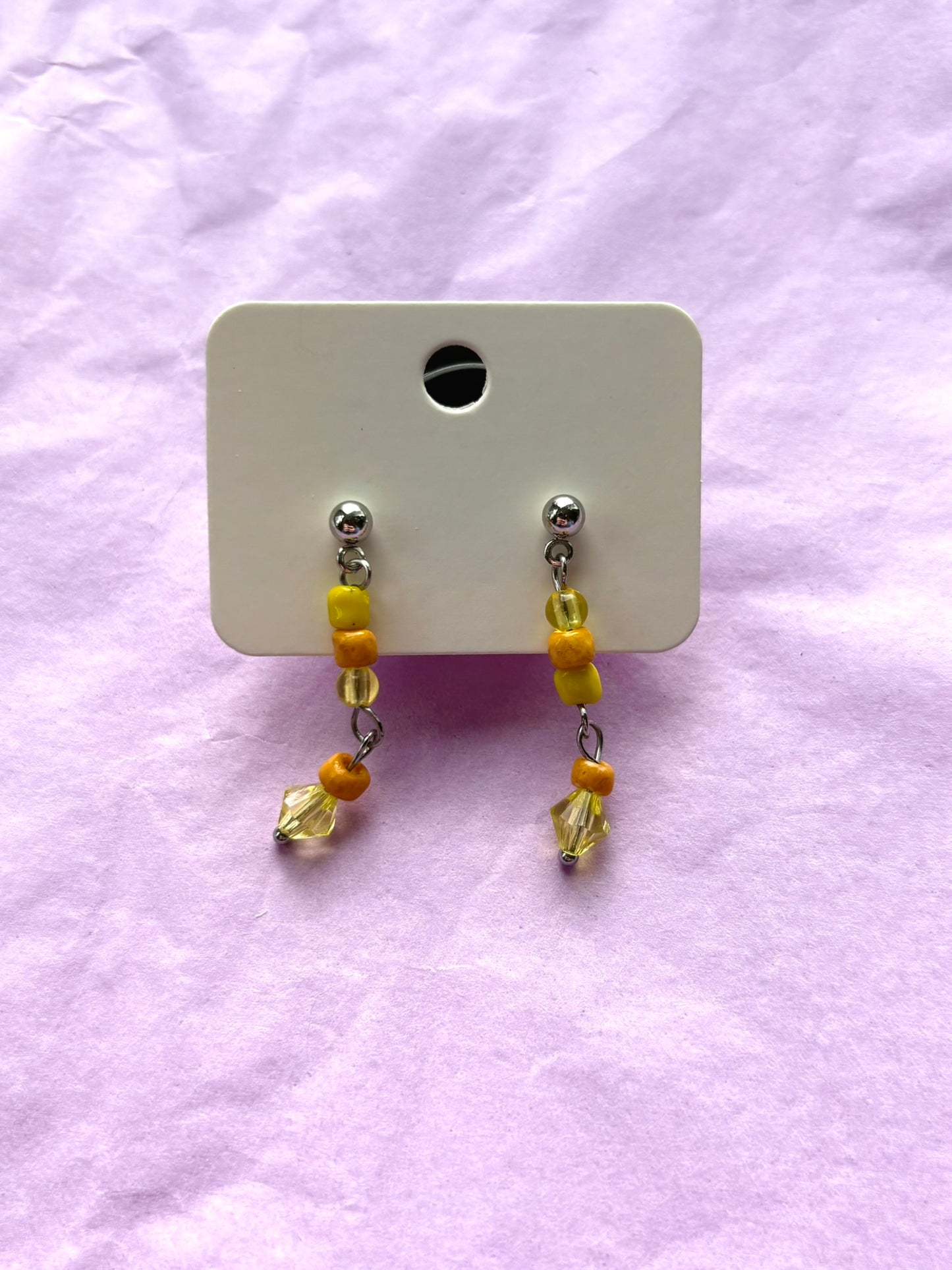 Pair of beaded earrings on a white card against a light purple background