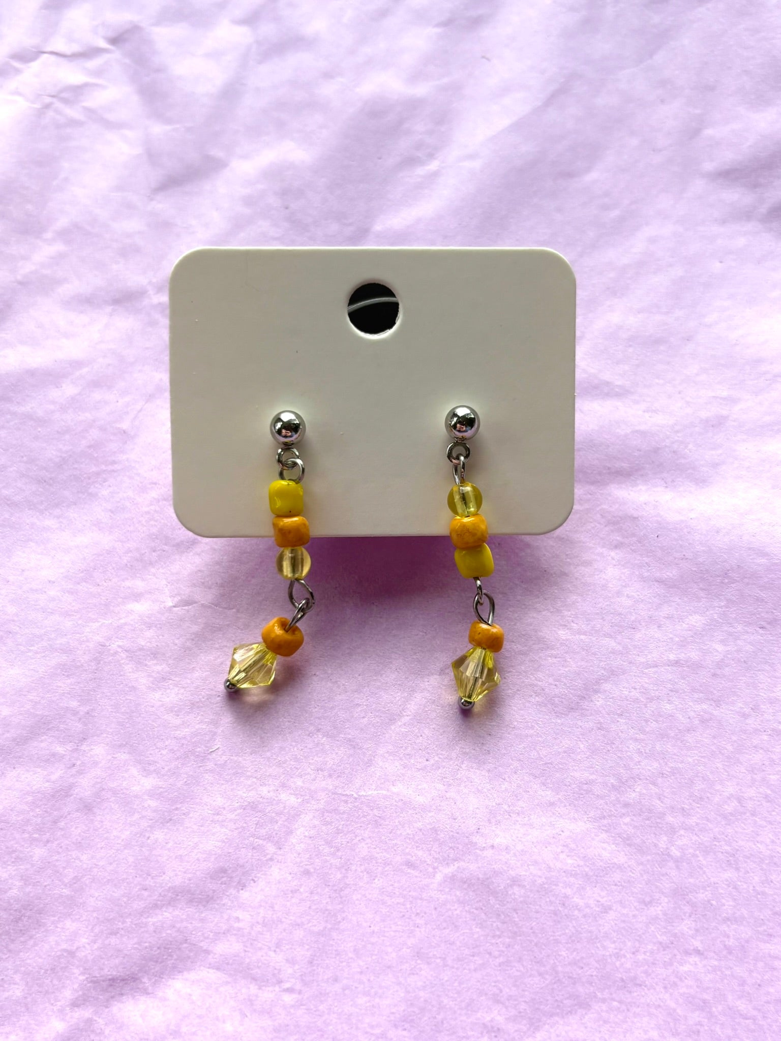Pair of beaded earrings on a white card against a light purple background